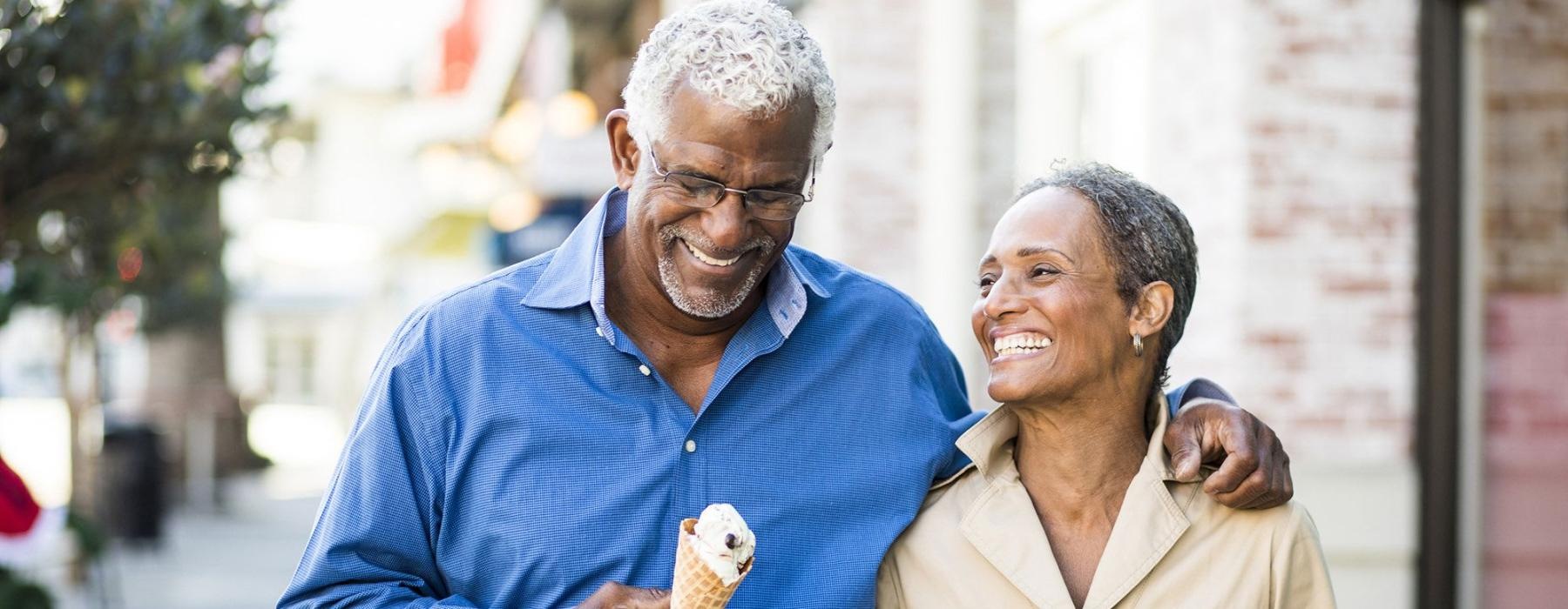 older couple walks down city sidewalk while holding ice cream cones